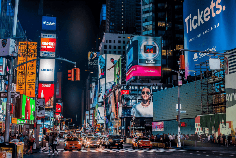 Bright neon signs and billboards lighting up Times Square with busy traffic below.
