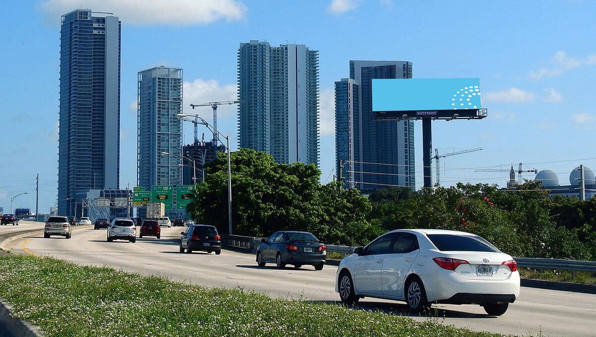 miamia-highway Urban road with vehicles driving toward tall skyscrapers, featuring an empty billboard space on the side.