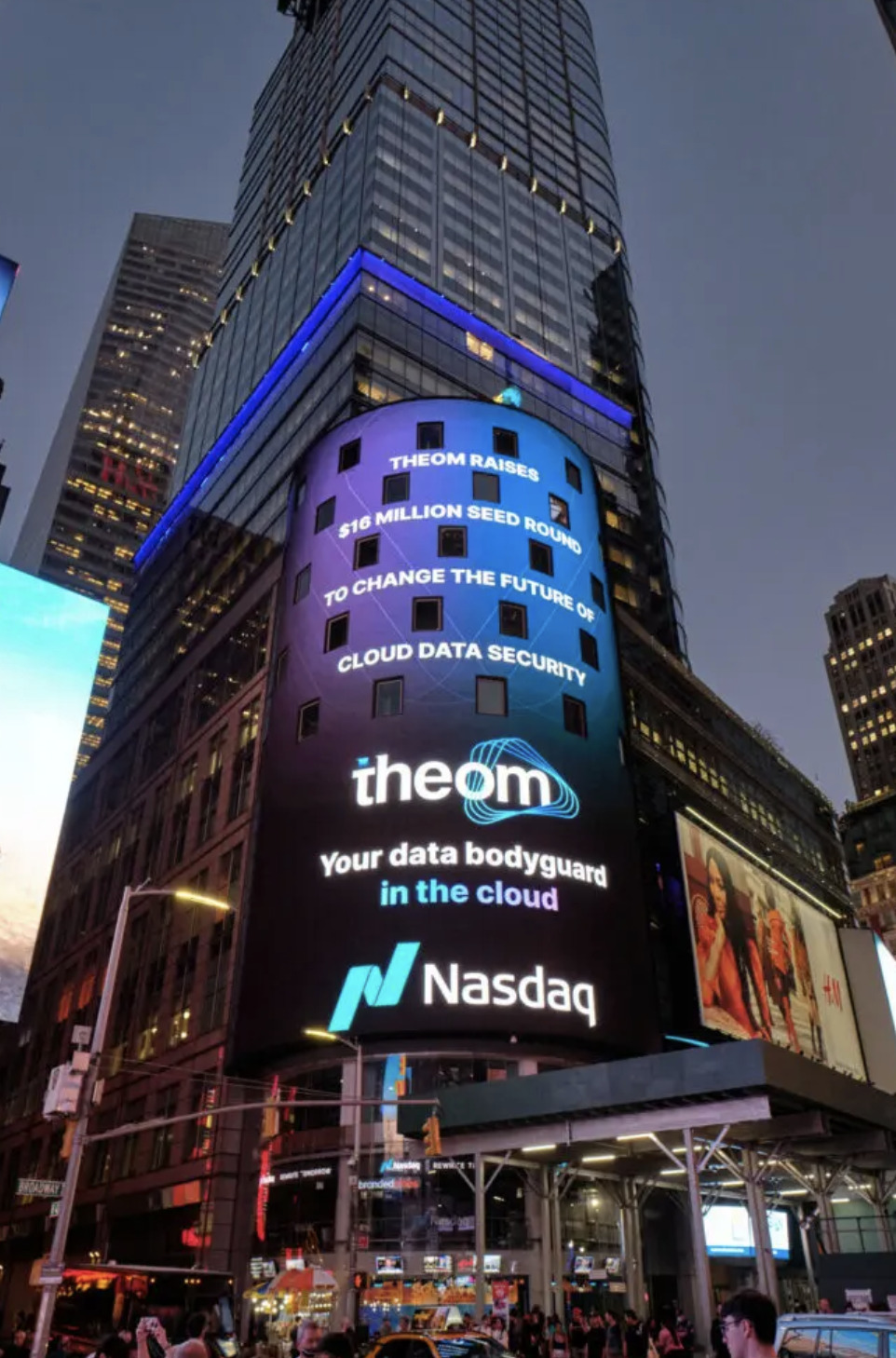 Evening billboard in Times Square for Theom, showcasing its cloud security message alongside Nasdaq branding.